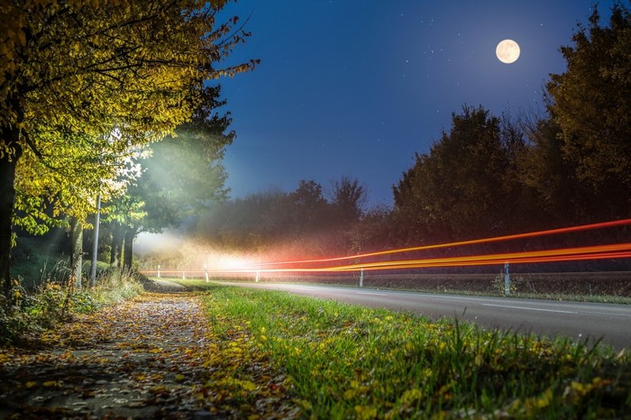 Night road with light trails and full moon