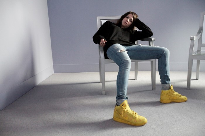 K. Flay sitting in a chair wearing ripped jeans and yellow sneakers