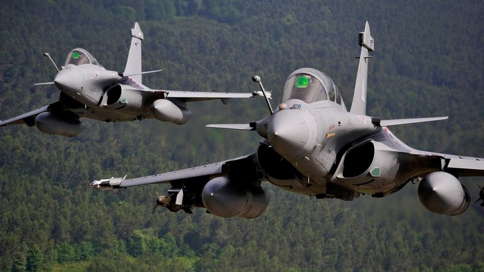 Two Dassault Rafale fighter jets flying over a forest