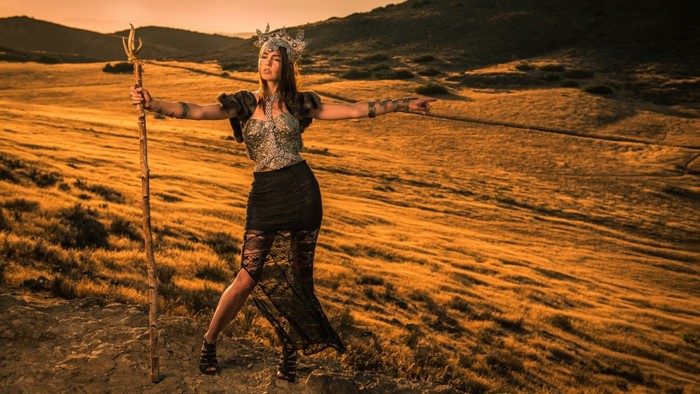 Woman in costume holding a staff in a field at sunset