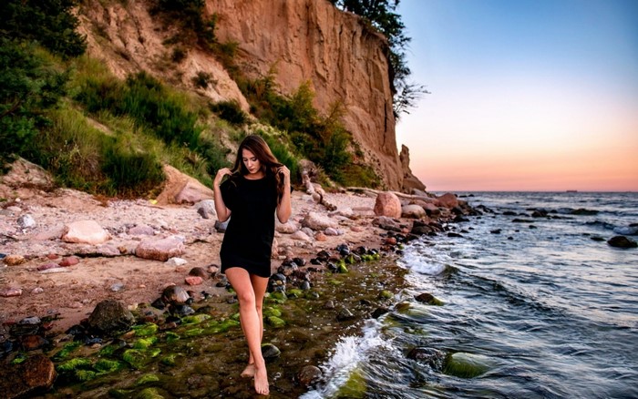 Woman in black dress on a rocky beach at sunset