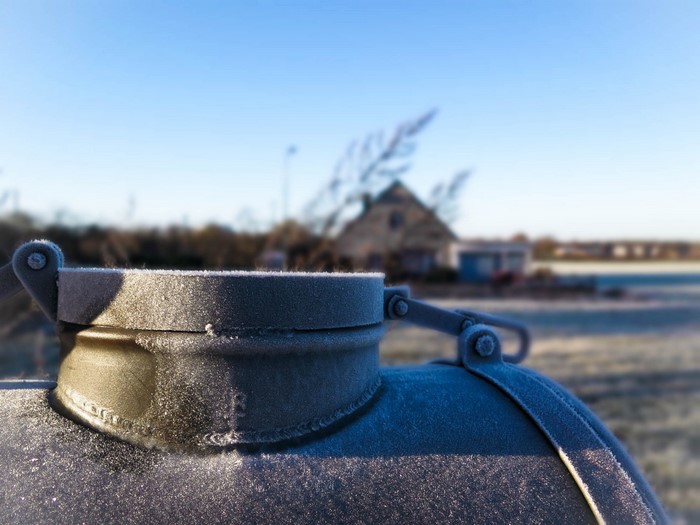 Frozen metal cap on a tank with a house in the background