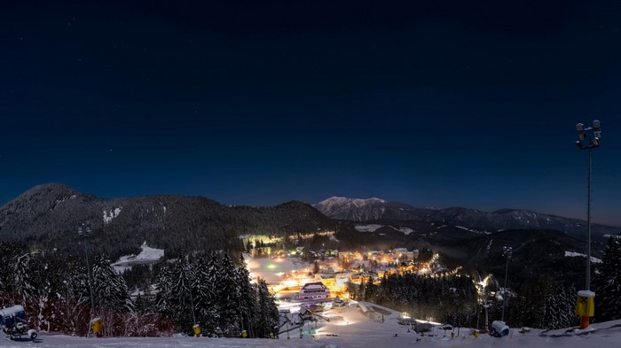 Night view of a snowy mountain resort with illuminated buildings and stars