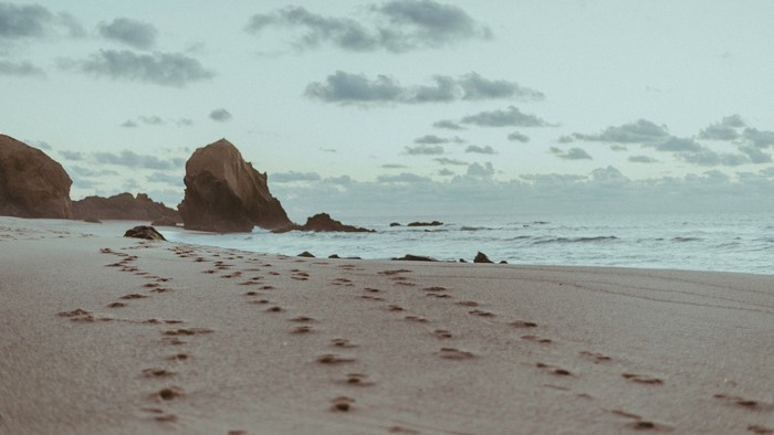 Footprints on a sandy beach with rocks and ocean waves