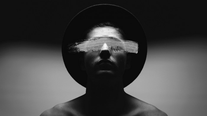 Man wearing a hat with white paint over his eyes