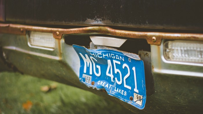 Bent Michigan license plate MG 4521 on a rusty bumper