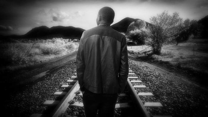 Man standing on railroad tracks in monochrome landscape