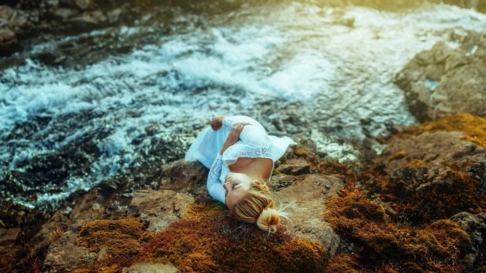 Woman in white dress lying on rocks by water