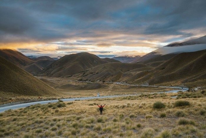 Person with arms raised in a valley with rolling hills