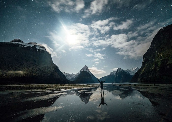 Person with arms raised in a fjord at night
