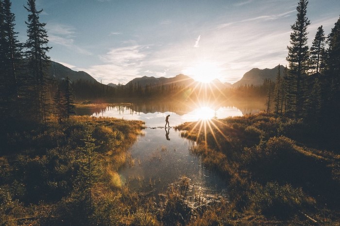 Person walking on rocks across a lake at sunrise