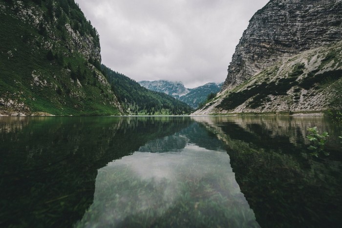Lake reflecting mountains and green hills under a cloudy sky
