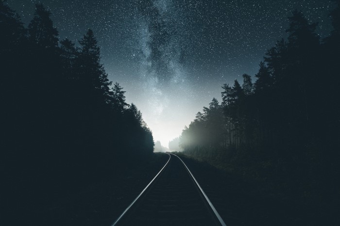 Railway through a forest under the starry night sky