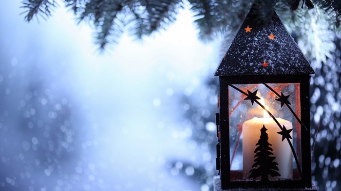 Lit lantern with candle and Christmas tree silhouette in snow