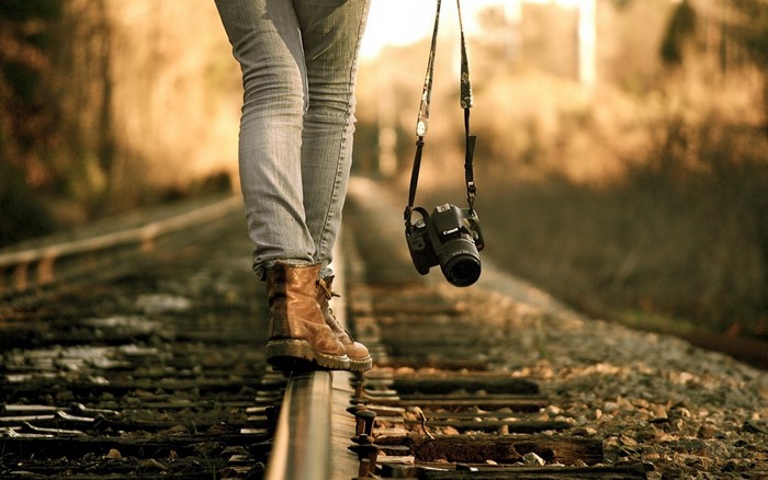 Person walking on railroad tracks with a camera