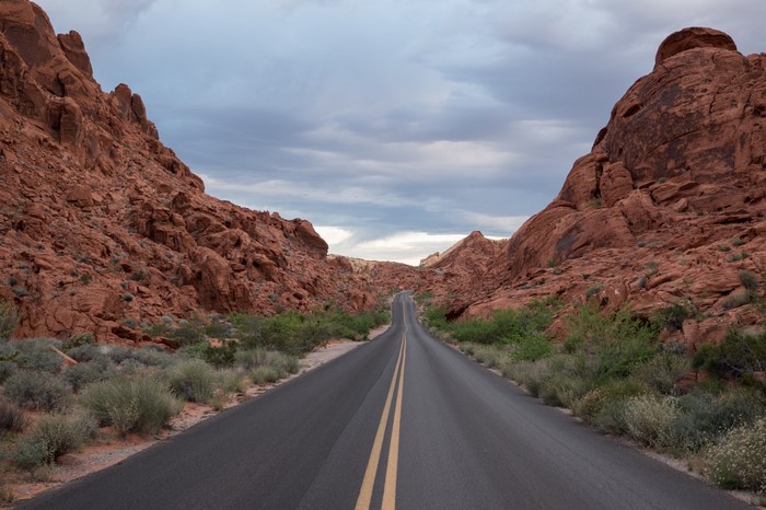 Desert road through red rock formations under cloudy sky