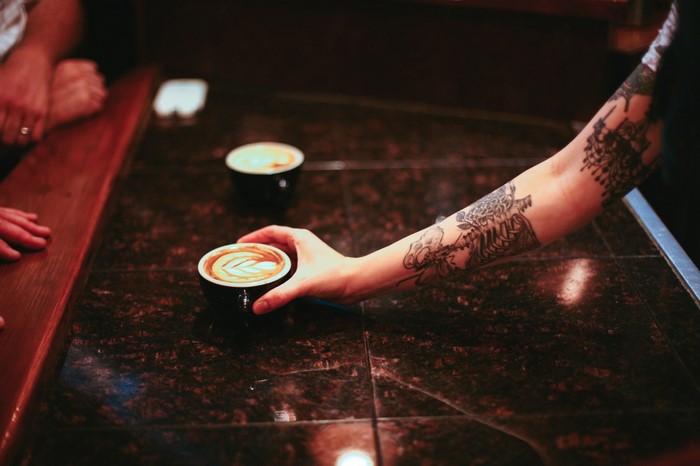 Tattooed arm holding latte art coffee cup