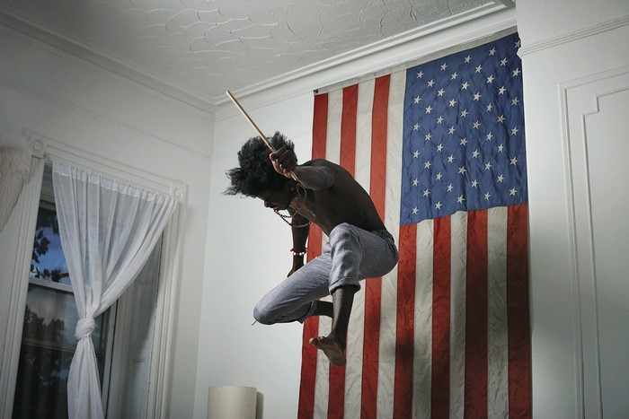 Man with drumstick jumping in front of American flag