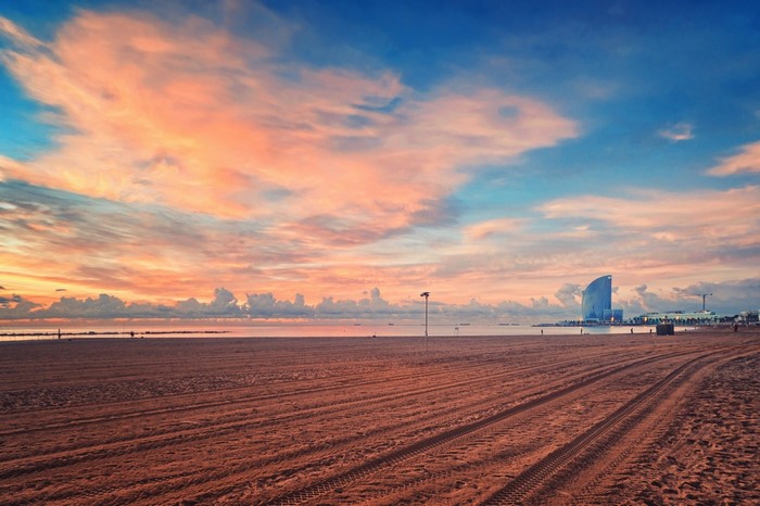 Beach at sunset with clouds and a building in Barcelona