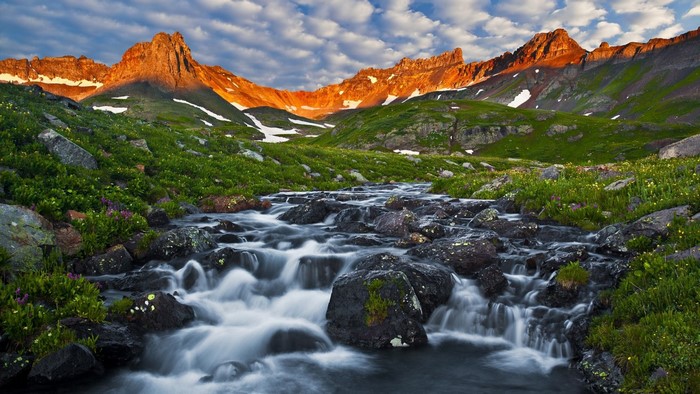 Mountain stream flowing through a green valley at sunrise