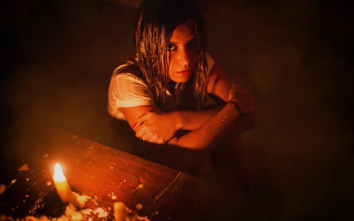Woman sitting in darkness with candles