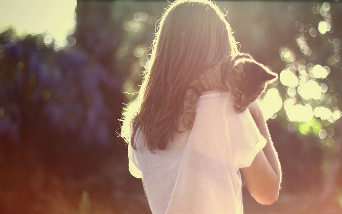 Girl holding a cat on her shoulder outdoors