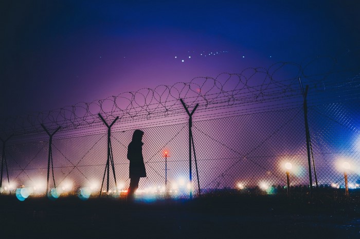 Silhouette of a person by a barbed wire fence at night