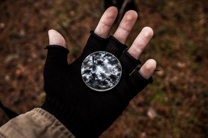 Hand wearing black fingerless glove holding a round object with reflection