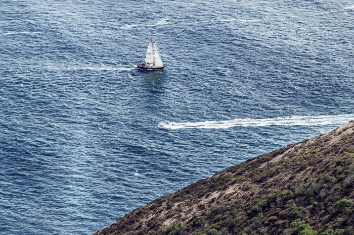 Sailboat and motorboat on the ocean near a hill