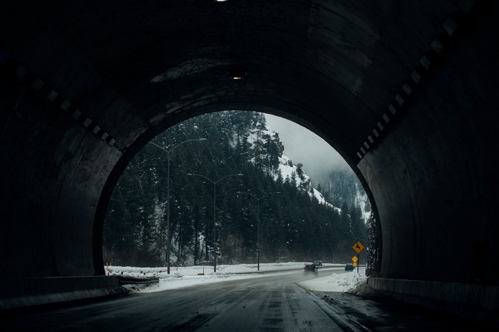 View from a tunnel exit onto a snowy mountain road