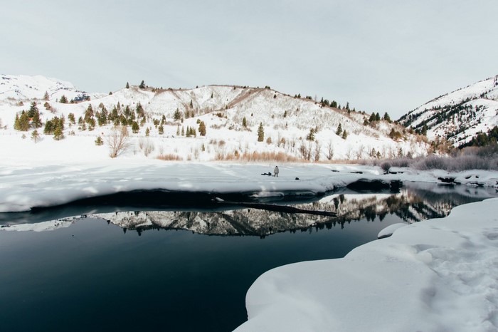 Snowy mountains and a partially frozen river with reflections