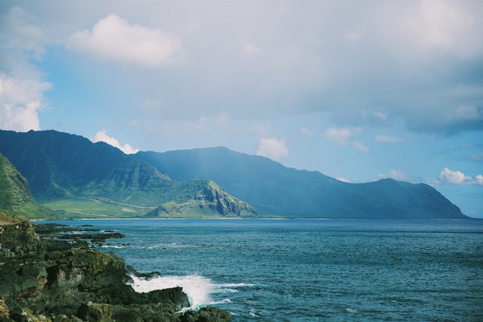Ocean waves crash against rocky coast with mountains in background