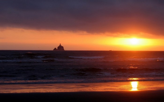 Sunset over the ocean with a lighthouse on a rock