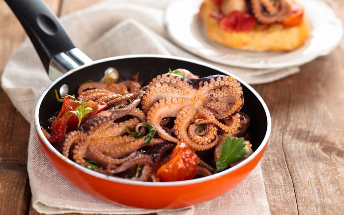 Octopus dish with tomatoes and herbs in a pan