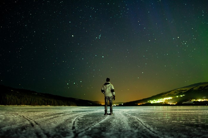 Man standing on frozen lake under starry night sky in Norway