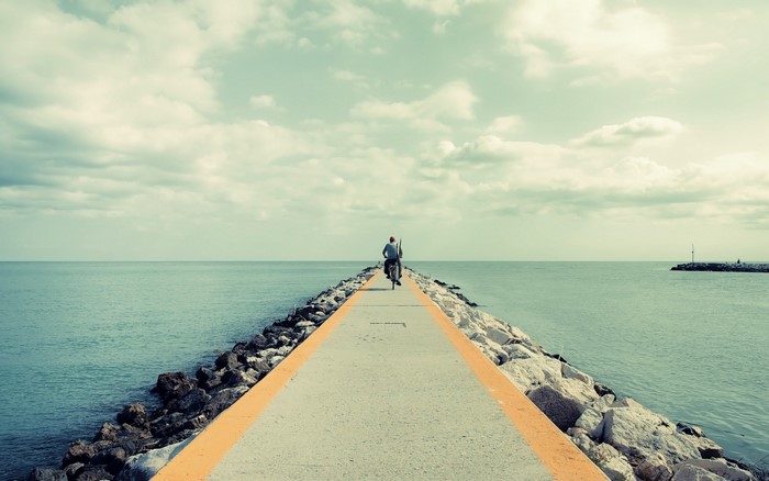 Person riding a bicycle on a pier over the sea