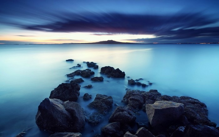 Rocky shore at dusk with distant mountain and clouds