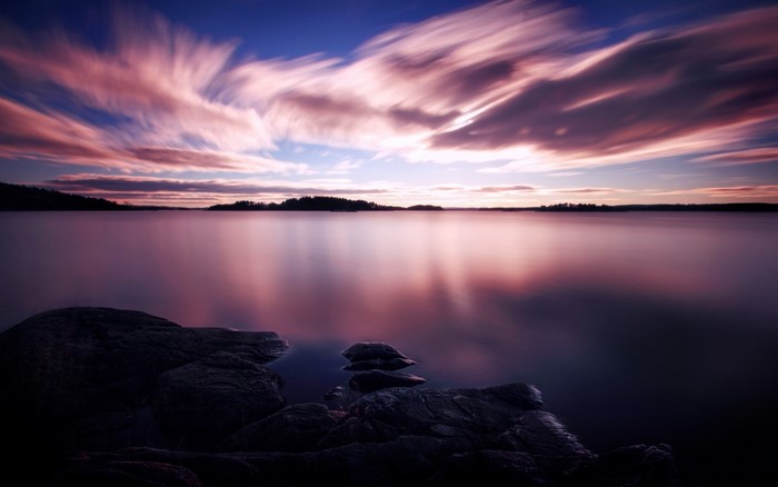 Long exposure of clouds over a calm lake at sunset
