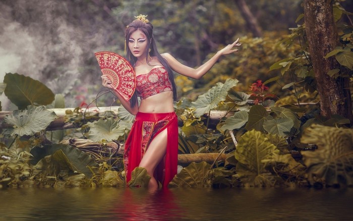 Asian woman in traditional attire holding a fan in a forest
