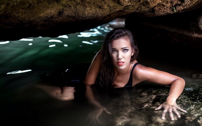Woman in black swimsuit in a cave with water