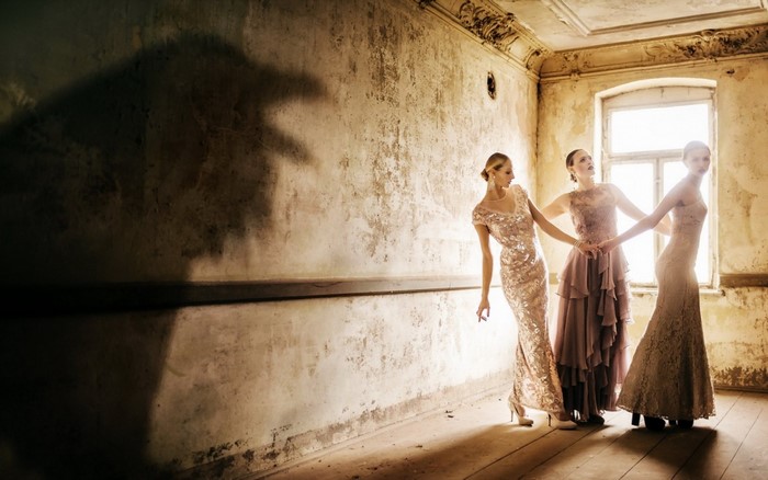 Three women in elegant dresses in a derelict room with a shadow