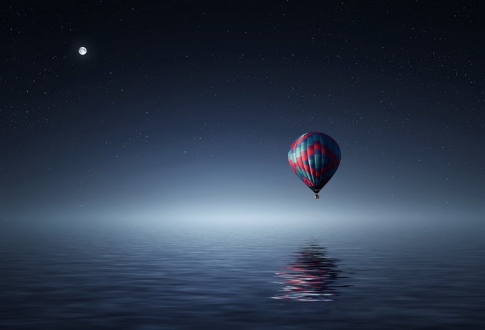 Hot air balloon over water at night with moon and stars
