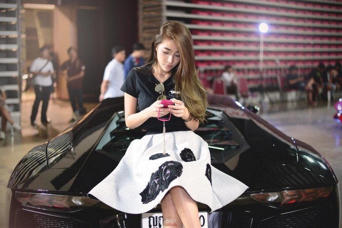 Woman sitting on a black Lamborghini at an auto show