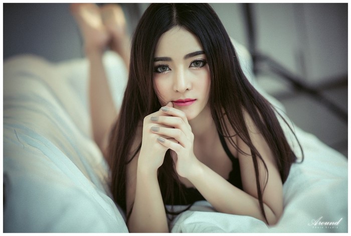 Asian woman with long dark hair lying on a bed