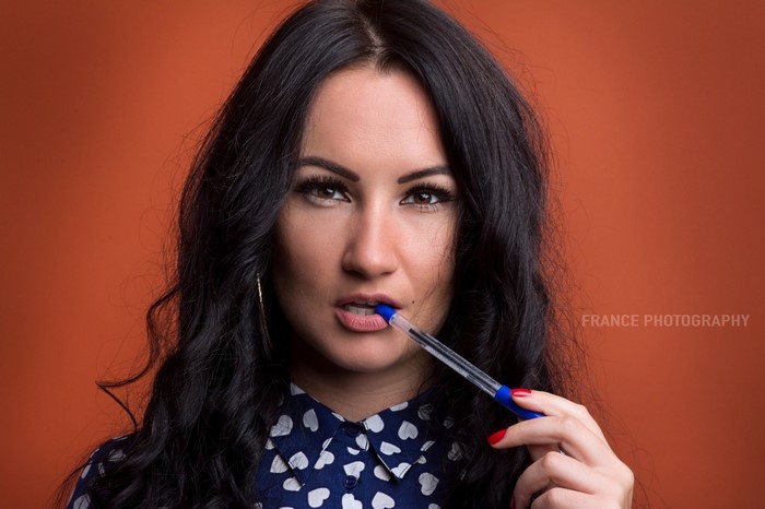 Woman with black hair holding a pen to her mouth