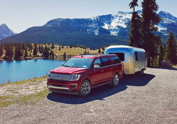 Red Ford Expedition towing Airstream trailer near lake and mountains