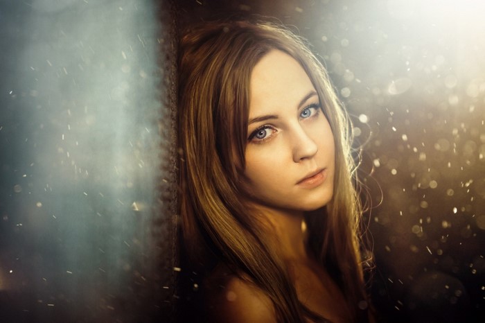 Woman with brown hair and blue eyes leaning against a wall