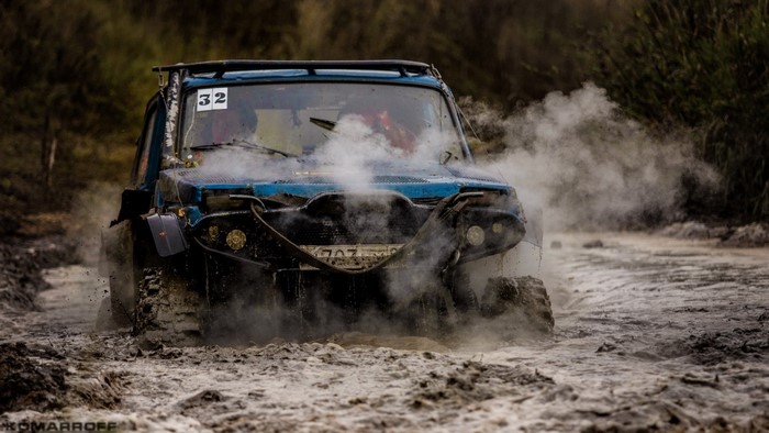 Blue offroad vehicle racing through mud and smoke