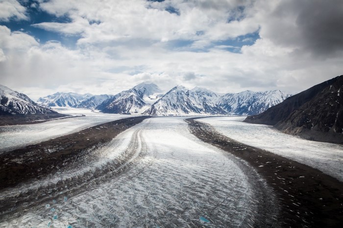 Expansive glacier valley with snow-capped mountains under a cloudy sky