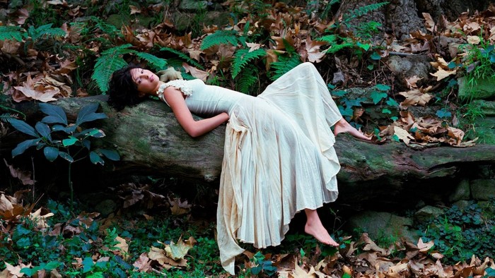 Woman in a white dress lying on a fallen tree in a forest